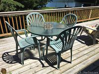 Patio set on wooden deck with round 40-inch glass table and four green plastic chairs in useable outdoor condition.