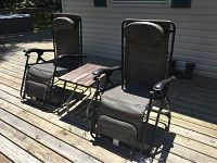Photo of two antigravity chairs and a small side table on a wooden deck in sunlight.