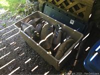 Beige Rubbermaid container with six duck decoys inside, positioned outdoors on ground with sunlight and shadows.