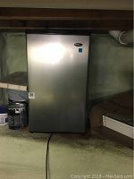 Front view of stainless steel Danby bar fridge with black sides, showing the closed door in a basement setting.