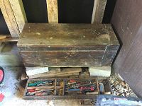 Closed vintage wooden tool box with shelf bottom, aged surface, resting on concrete blocks.