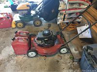 Image showing red Tecumseh gas lawn mower with two red gas containers placed beside it on the ground.