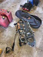 Snowshoes, poles and carrying case displayed on a cement floor next to some red gas cans.