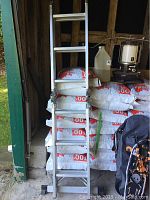 Full front view of the aluminum ladder leaning against stacked bags inside a storage area.