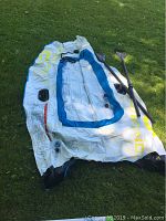Blue and white inflatable dinghy laid on grass with two black paddles alongside.