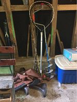 Fishing net with long handle, ice fishing auger with blue blades, and chest waders with rubber boots in barn interior