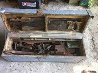 Open view of vintage wooden toolbox filled with assorted hand tools such as handsaws, levels, hand planes, and large drill bits.