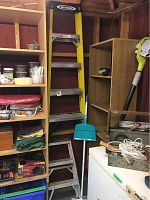 5ft yellow Werner fiberglass step ladder next to shelving and a tall green and white handled cleaning tool in the corner of a room with wood walls