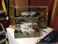 Wooden tool box full of several hand tools including vintage metal hand planers, alongside a small metal toolbox containing various small parts and tools with a rope on top