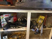 Photo showing Skil hammer drill in box and loose, along with charger and cord, wrenches and other tools stored on shelf.