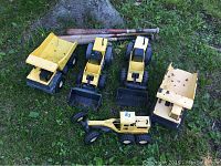 Five yellow metal Tonka trucks with three wooden baseball bats on grass, showing age wear and rust