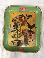 Photo of the front side of the vintage Coca Cola metal tray showing the Coca Cola bottle and floral bouquet design on a yellow background with green border and red Coca Cola logos.