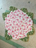 Photo showing the full hooked rug shaped like a flower with green leaves around edges and a densely packed pink and white floral pattern in the center.