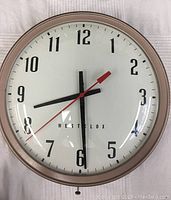 Front view of vintage Westclox wall clock showing white face, black numbers, and red second hand.