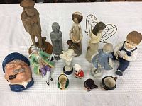 Thirteen assorted figurines arranged on a white cloth surface showing variety in style and theme