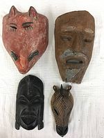 Four carved wood masks laid out on a white surface, showing design and color details.