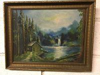 Framed oil painting showing full view of a cabin by the river with pine trees and distant waterfall.