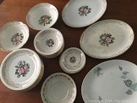 Wide view showing a grouped assortment of the Tudor Rose patterned dishes including platters, bowls, plates, and saucers with gold trim.