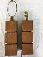 Pair of tall wood block table lamps on a white cloth background, front view.