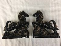 Pair of black and gold horse figurines facing each other on white fabric background.