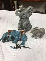 Elephant lot with gray cast iron and ceramic elephants and toy elephants showing all items on white cloth background.