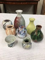 Eight different miniature pottery items displayed on a white surface with a decorative wooden table in the background.