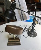 Two desk lamps shown with cables. One articulated black metal lamp with round base and the other vintage style brown lamp with rectangular base.