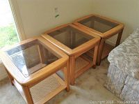 Three oak end tables with beveled glass tops and cane shelves below, positioned on carpet adjacent to sofa