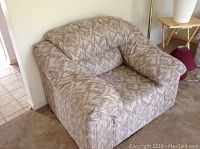 Side view of the patterned upholstered chair showing cushioned backrest, armrest, and seat