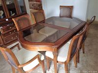 Dining set showing antique finish wooden table with bevelled glass inset top and six cane back dining chairs with upholstered seats.