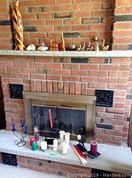 Wide shot of fireplace mantel displaying nine brass figurines, three carved wood art pieces, and two pewter figures on stone bases.