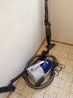 Kenmore canister vacuum placed on floor with hose and nozzle coiled nearby against a wall.