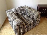 Front left angled view of the striped upholstered armchair on beige carpet next to a wooden side table.