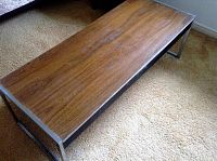 Photo of a rectangular coffee table showing the brown MDF top with visible water damage and metal frame.