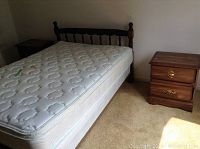 Double wooden bed frame with spindle headboard and mattress next to an MDF night table with two drawers.