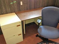 Desk with Arborite top next to filing cabinet inside room with wood-paneled walls and carpet