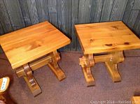 Photo showing two pine wood end tables with a natural finish and visible wood grain and knots, placed side by side against a wood-paneled wall.