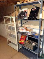 Two metal shelving units in a basement setting, one light gray and one gray, showing wear and partially filled with various items.