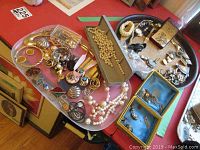 Pink and black trays holding assorted bracelets, necklaces, pins, earrings, watches