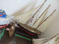 Photo showing both model ships side-by-side, highlighting the larger schooner model with sails and the smaller wooden model with mast only.