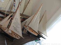 Three medium-sized wooden sailboat models with fabric sails displayed on a table.