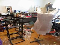 Full view of the dress form and wooden valet stands in a cluttered room with various items around them.