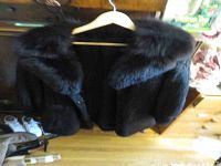 Front view of black fur coat on wooden hanger against dresser.
