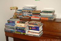 Photo showing stacks of books primarily on military history and airplanes arranged on a piano with a brass metal piano lamp on top.