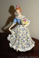 Front view of porcelain figurine of woman in floral dress with bouquet and dog.