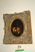 Full view of the framed vintage floral still life print, showing the ornate gold-toned floral and scroll detailed frame and the oval artwork inside.