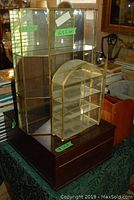 Photo showing a large hinged wooden box with dark finish, glass curio case with metal frame, and smaller arched metal frame display case on top