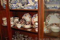 Wooden china cabinet displaying assorted vintage china pieces including cups, saucers, plates with blue and gold floral designs.