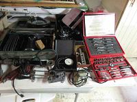 Wide angle showing all items on table including black Skil belt sander, boxed reamer sets, pressure gauges, soldering iron parts, and red tap and die set.