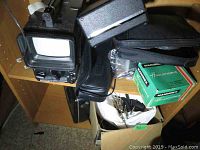 Overview of vintage electronics including small TV/projector screen, black cases and Hanimex film box on wooden shelf.